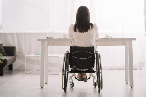 вид на бизнес-женщину, сидящую в инвалидной коляске рядом с столом в офисе
 - Фото, изображение