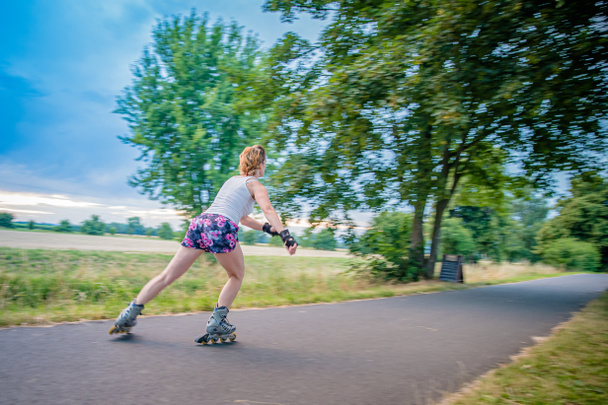 young woman rides on roller skates on an asphalt trail outside the city in summer - Photo, Image