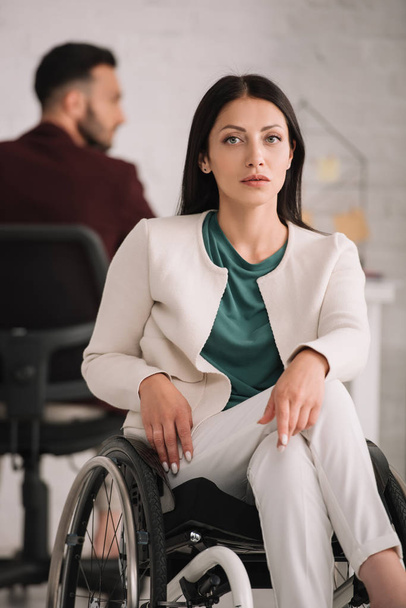 Selbstbewusste behinderte Geschäftsfrau blickt im Rollstuhl im Büro in die Kamera - Foto, Bild