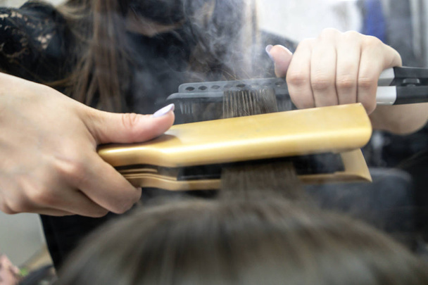 Cute girl with long brunette hair hairdresser doing hair lamination in a beauty salon. concept of hair care treatment, steam from hair - Photo, Image
