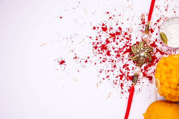 Ракша Бандхан фон с ракхи и разбросаны Кумкум и рисовое зерно на белом фоне с конфетами. Традиционный ракхи, который является символом любви между братьями и сестрами
 - Фото, изображение