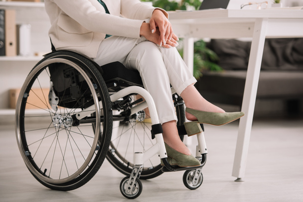 cropped view of disabled businesswoman sitting in wheelchair with crossed legs - Фото, зображення