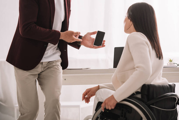 cropped view of manager showing smartphone with blank screen to disabled businesswoman - Foto, Imagem
