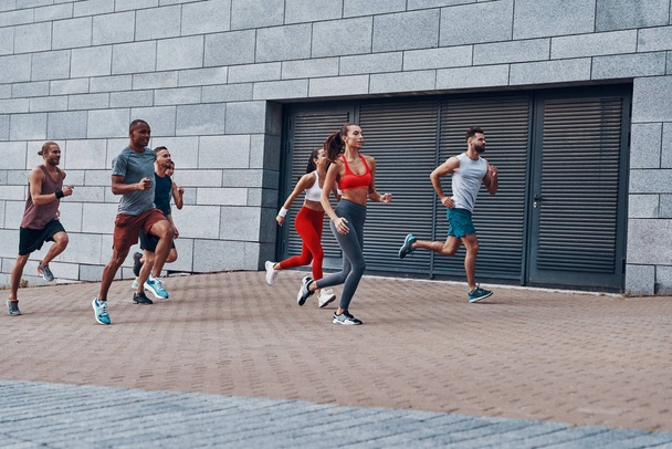 Grupo de jovens em roupas esportivas jogging enquanto se exercitam na calçada ao ar livre
            - Foto, Imagem