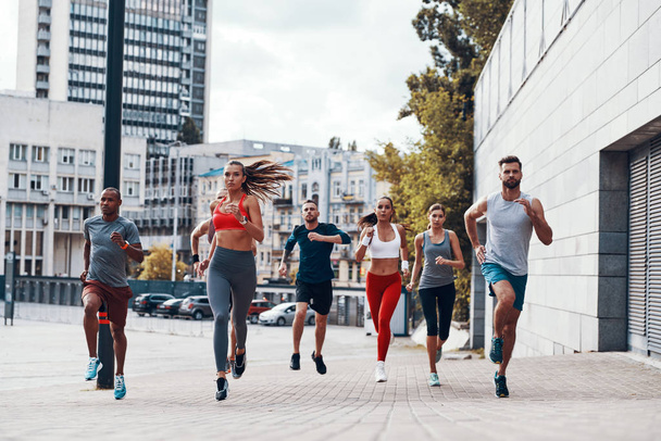 Full length of people in sports clothing jogging while exercising on the sidewalk outdoors                    - Foto, Imagen
