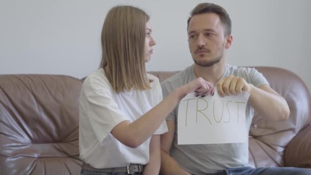 Man and woman tearing apart the word trust written on the paper. Problems in the relationship between man and woman. Betrayal, mistrust, breakup concept - Video