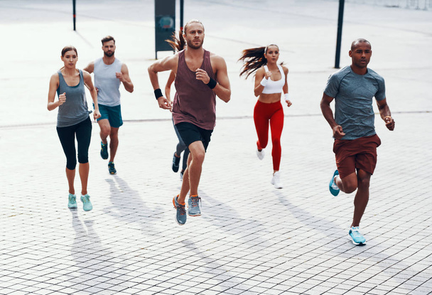 Full length of people in sports clothing jogging while exercising on the sidewalk outdoors                    - Foto, Bild