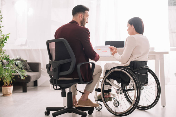 zdravotně postižena na invalidním vozíku zobrazující dokumenty obchodnímu partnerovi v kanceláři - Fotografie, Obrázek