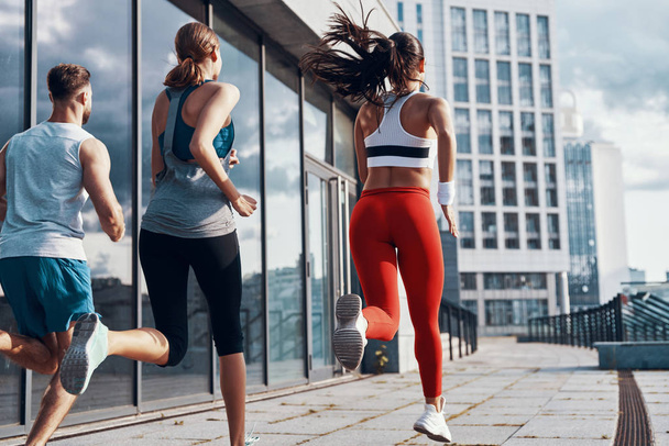 Vista trasera de las personas con ropa deportiva corriendo mientras hacen ejercicio en la acera al aire libre
  - Foto, imagen