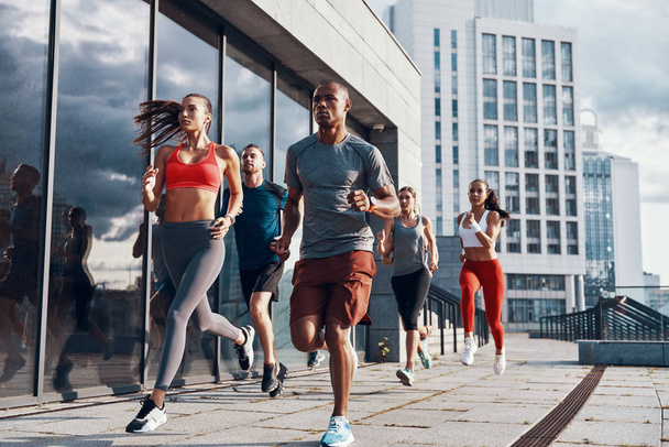 Group of people in sports clothing jogging while exercising on the sidewalk outdoors        - Foto, Bild