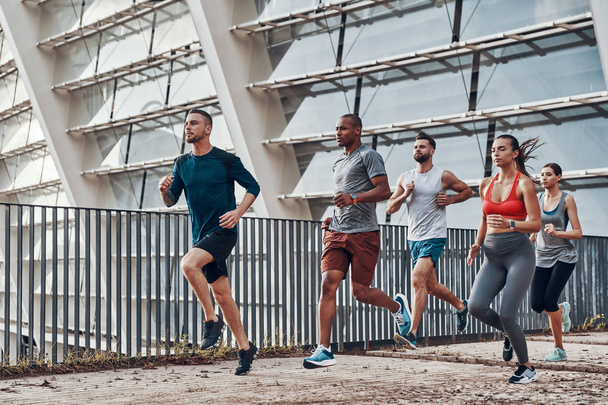 Group of young people in sports clothing jogging in city at Olympic stadium building  - Fotografie, Obrázek