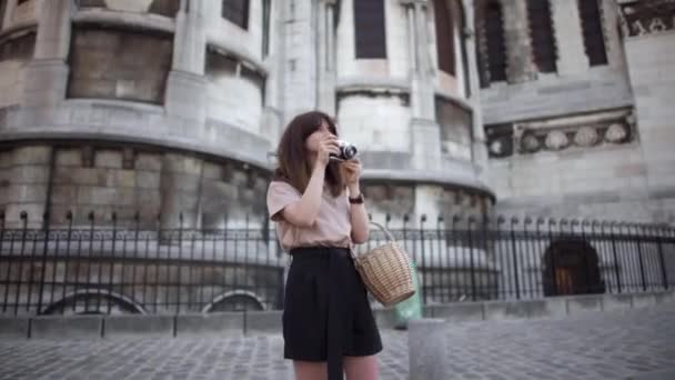Beautiful young woman with dark hair, dressed in black shorts and a beige t-shirt, takes pictures of the city. Right to left pan real time portrait shot. - Кадри, відео