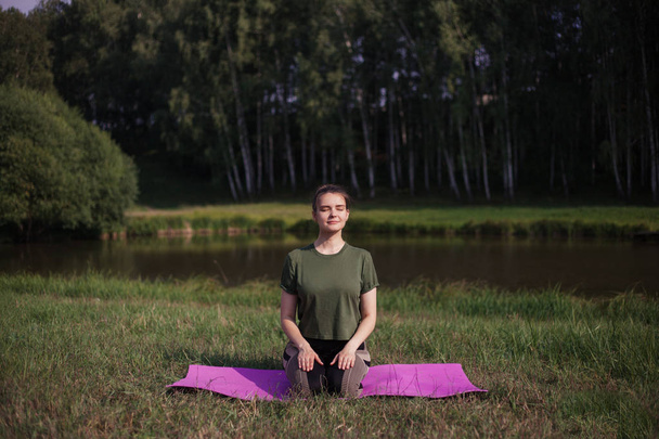 ein junges Mädchen übt Yoga in der Natur, in der Nähe des Sees - Foto, Bild