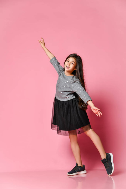 Full length beautiful little girl with long in gray dress and sneakers standing and posing on a pink background. - Foto, afbeelding