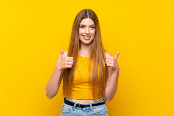 Young woman over isolated yellow background giving a thumbs up gesture - Photo, image