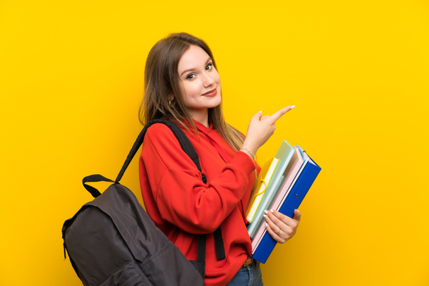 Adolescente estudante menina sobre fundo amarelo apontando dedo para o lado
 - Foto, Imagem