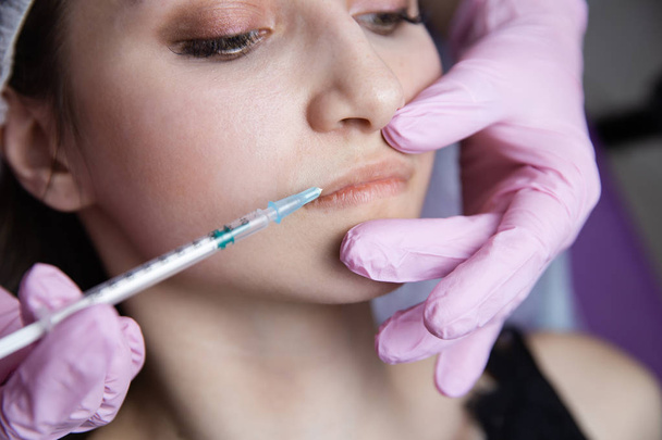 Le médecin cosmétologue effectue la procédure d'injections faciales rajeunissantes pour resserrer et lisser les rides sur la peau du visage d'une belle jeune femme dans une beauté
 - Photo, image