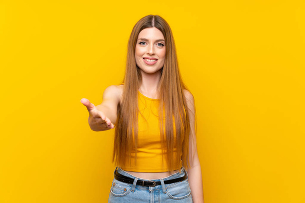 Young woman over isolated yellow background handshaking after good deal - Photo, Image