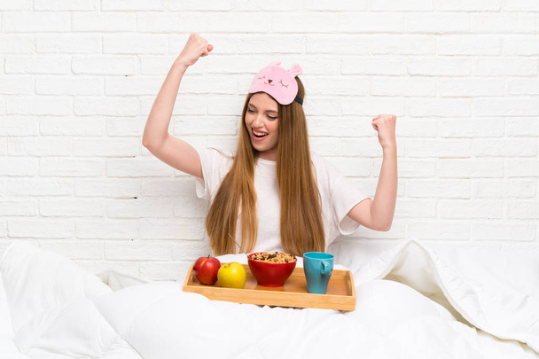 Young woman in dressing gown with breakfast celebrating a victory - Photo, Image
