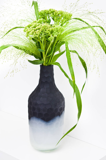 Grünes Gras und Feldblumen in einer modernen Onyx-Vase im Regal. - Foto, Bild