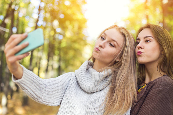 Dwie piękne młode kobiety robią selfie w jesiennym parku - Zdjęcie, obraz