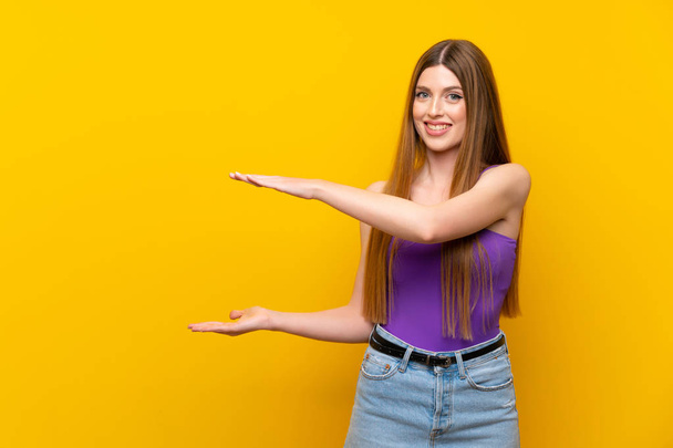 Young woman over isolated yellow background holding copyspace to insert an ad - Photo, Image