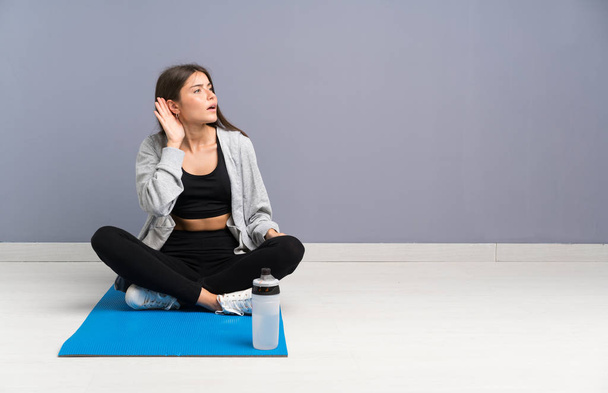Young sport woman sitting on the floor with mat listening something - Photo, image