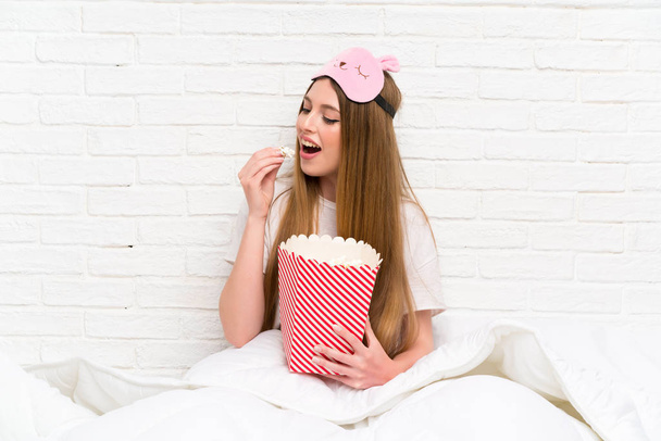 Young woman in dressing gown in bed holding popcorns - Photo, image