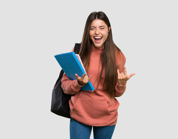 Young student woman holding notebooks making rock gesture over isolated grey background - Photo, Image