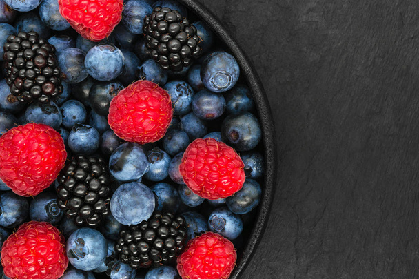 Various berries in round and black cast iron bowl - Foto, Imagen