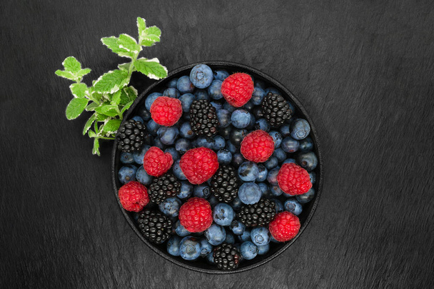 Különböző bogyós gyümölcsök kerek és fekete öntöttvas tálban - Fotó, kép