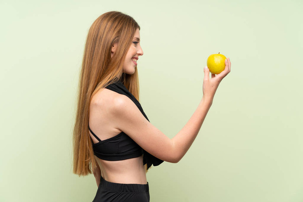 Young sport woman over isolated green background with an apple - Photo, Image