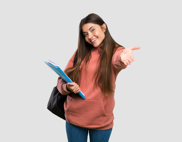 Jeune étudiante tenant des cahiers présentant et invitant à venir avec la main sur fond gris isolé
 - Photo, image