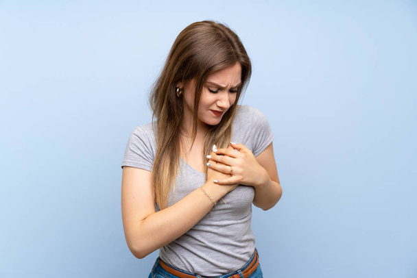 Έφηβο κορίτσι πάνω από απομονωμένο μπλε τοίχο που έχει έναν πόνο στην καρδιά - Φωτογραφία, εικόνα