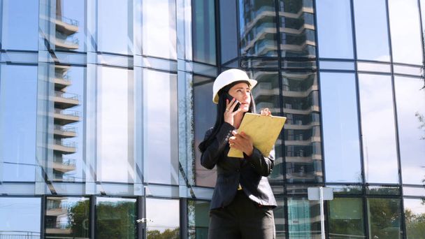 Female contractor in helmet with folder. Building, developing, construction and architecture. Concept of: Woman, Business, Skyscraper, Business plan, Work, Lifestyle, Beautiful. - Foto, immagini