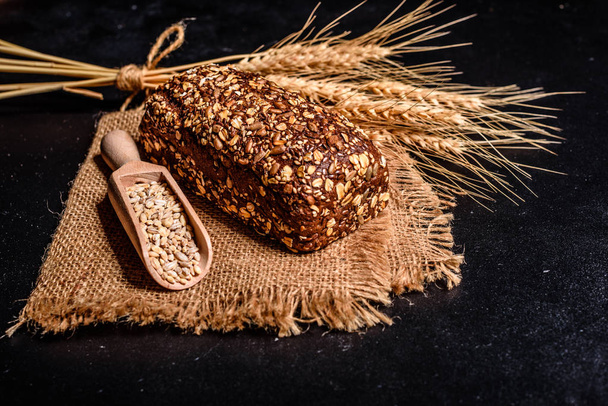 Pane fresco e profumato con chicchi e coni di grano su sfondo scuro. Assortimento di pane al forno su fondo tavola in legno
 - Foto, immagini