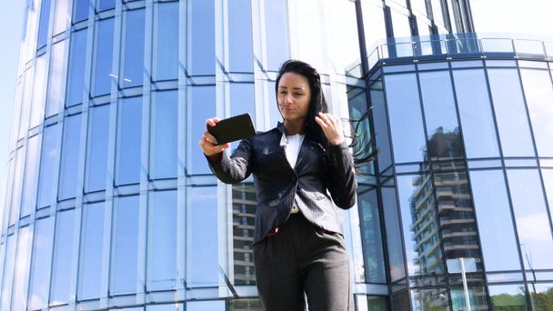 Businesswoman making selfies in front of office building. Smiling lady taking photos for her business partners abroad. Concept of: Lifestyle, Mobile, Selfie, Alone, Summer. - Фото, изображение