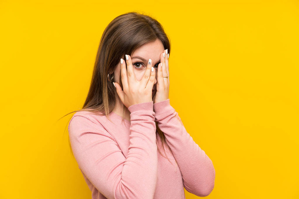 Dívka na izolovaném žlutém pozadí zakrývající oči a procházející prsty - Fotografie, Obrázek