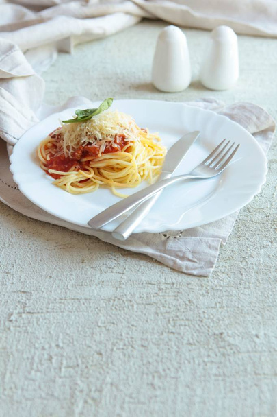 Pasta Fettuccine Bolognese with tomato sauce on white plate. Carlic and salt and tomatoes on a concrete background with linen napkins. - Фото, изображение