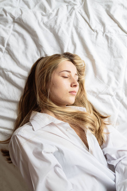 Portrait beautiful blonde woman with a beautiful face and amazing eyes, lies, sleeps on the bed linen in an elegant. And sensual looks and flirtatious smile. Health and harmony concept - Foto, Imagen