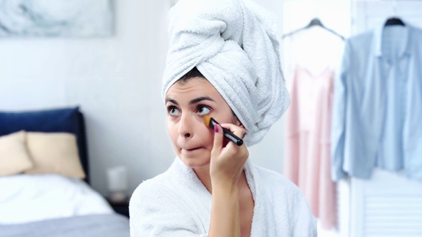 жінка в халаті наносить макіяж фундаменту косметичним пензлем
 - Кадри, відео