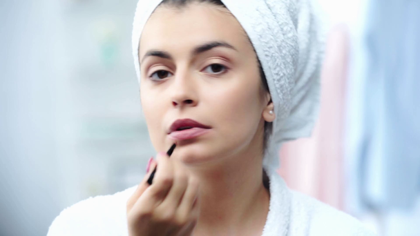 mujer en albornoz aplicando lápiz labial con cepillo cosmético
 - Metraje, vídeo