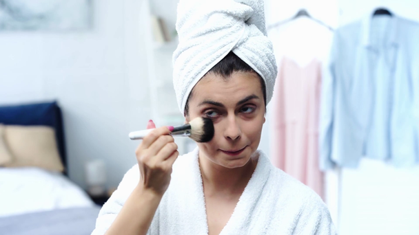 mujer en albornoz aplicando polvo facial con cepillo cosmético
 - Metraje, vídeo