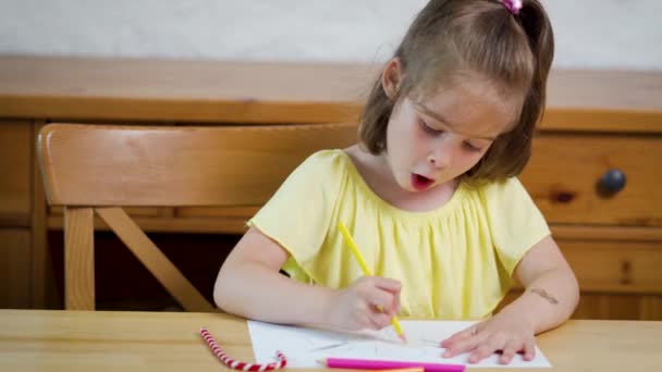 mała dziewczynka w żółtej sukni z kredkami rysuje na papierze - Materiał filmowy, wideo