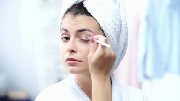 mosolygós nő fürdőköpeny alkalmazása szemhéjfesték a kozmetikai kefe - Felvétel, videó
