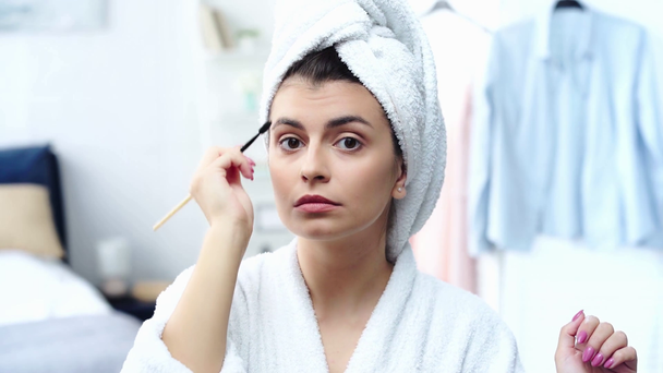 mujer sonriente en bata de baño estilo cejas con cepillo cosmético
 - Metraje, vídeo