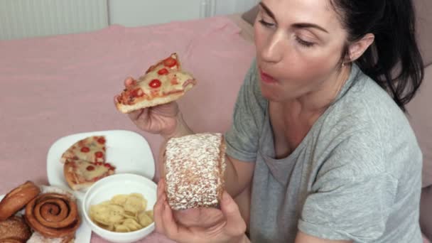 Vrouw eet zoete broodje en een stukje pizza. Slecht ongezond eten voedings concept - Video