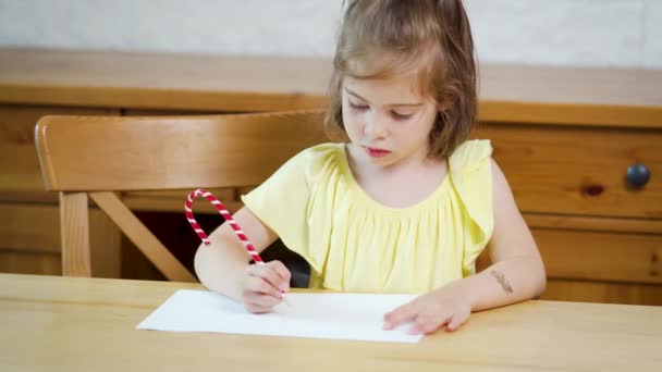 klein meisje in een gele jurk met een potlood trekt op papier - Video
