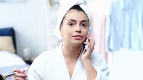boldog asszony a fürdőköpeny alkalmazása arcát por és beszél a smartphone - Felvétel, videó