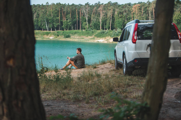 uomo seduto vicino bianco suv auto al bordo guardando il lago con acqua blu
 - Foto, immagini